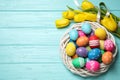 Colorful Easter eggs in decorative nest and tulip flowers on light blue background, flat lay. Space for text Royalty Free Stock Photo