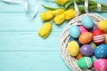 Colorful Easter eggs in decorative nest and tulip flowers on blue wooden background, flat lay. Space for text Royalty Free Stock Photo