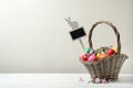 Colorful Easter eggs, flowers and tag in wicker basket on white wooden table against background. Space for text Royalty Free Stock Photo