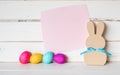 Colorful Easter Eggs with Pink Paper Invite Card and a Simple Bunny against White Shiplap Board Background wall