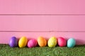 Colorful Easter Eggs In Row On Bottom Of Pink Wood Boards Wall Background And Laying In Green Grass With Room Or Space For Copy