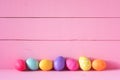 Colorful Easter Eggs in a Row on a Table and against a Bright Pink Board Wall Background with copy space. Horizontal and wide with