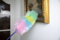 Colorful feather duster wiping the dust from oil painting in modern white home, Cleaning concept. Dust on vintage