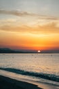 Colorful fiery orange evening sunset on ocean. Silhouettes of surfers in calm sea waves against cloudy sky painted in Royalty Free Stock Photo