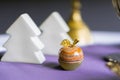 Colorful figurine of apple made of onyx on violet table with white fir tree figurines on background