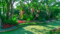 Colorful flowering plant and green grass lawn under group of trees in a good care maintenance garden, wooden curve walkway