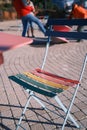 a colorful folding chair sits alone on a street corner while people walk by