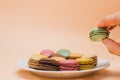 Colorful French macaroons on an apricot background, One green cake held in your fingers, As if greedily taken from a plate, Place Royalty Free Stock Photo