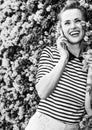 Happy trendy woman near flowers bed talking on cell phone