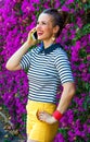 Smiling trendy woman near flowers bed speaking on cell phone