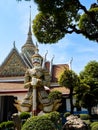 Colorful giant demon guardian statue at Wat Arun Temple in Bangkok, Thailand, framed by green trees and a blue sky