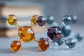 Colorful glass molecular models in orange, yellow, and blue arranged on a light surface with blurred books in the background Royalty Free Stock Photo