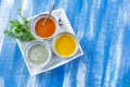 Colorful green, yellow and red spicy sauces in bowls in a white plate isolated on blue wooden painted plank Royalty Free Stock Photo