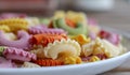 Colorful green, yellow, white, orange and pink italian crown pasta on white plate staying on wooden table, close-up.