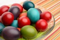 Colorful hand dyed easter eggs in a bowl on a table with striped tablecloth.