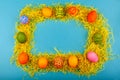 Colorful handmade Easter eggs in a frame made of dry grass. The view from the top.  on a blue background Royalty Free Stock Photo