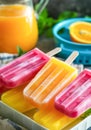 Colorful Homemade Fruit Popsicles on a Summer Day With Fresh Orange Juice in the Background