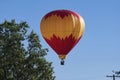 Red and Yellow Hot Air Balloon Descending Close to a Tree Royalty Free Stock Photo