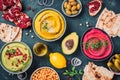 Colorful hummus bowls - green, yellow and beetroot hummus on dark background with lemon, olive oil, sesame seeds, pita, raw