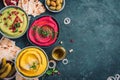 Colorful hummus bowls - green, yellow and beetroot hummus on dark background with lemon, olive oil, sesame seeds, pita, raw