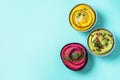Colorful hummus bowls - green, yellow and beetroot hummus on dark background with lemon, olive oil, sesame seeds, pita, raw