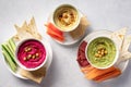 Colorful hummus in bowls, served with vegetables sticks and crackers.