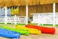 Colorful kayaks on white sand on the beach of Cyprus against summer house with white wooden fence and reed roof