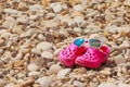 Colorful kids sandals on a pebble beach. kid`s summer plastic shoes and summer sunglasses on the rocky beach. Copy space Royalty Free Stock Photo