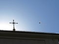 Colorful Kite with a Long Tale Flying over a Roof of Church with Cross on Top in Sun Royalty Free Stock Photo