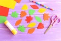 Colorful leaves cut from colored paper, scissors, glue stick, pencil, paper sheets on purple wooden background. Top view