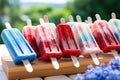 A colorful lineup of frozen treats resting on a solid wooden surface., Red, white, and blue popsicles on an outdoor table, AI