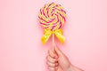 Colorful lolipop with pink, yellow and white spiral in hand on pink background