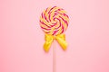 Colorful lolipop with wooden stick, pink, yellow and white spiral on pink background , childhood sweets