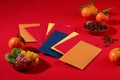 Colorful lucky money envelopes, a plate of dried fruit, a plate of melon seeds and tangerines are placed on a red background.