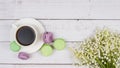 Colorful macaroons, a cup of coffee and lilies of the valley on wooden background, close-up flat lay Royalty Free Stock Photo