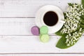 Colorful macaroons, a cup of coffee and lilies of the valley on wooden background, close-up flat lay Royalty Free Stock Photo