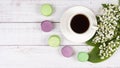 Colorful macaroons, a cup of coffee and lilies of the valley on wooden background, close-up flat lay Royalty Free Stock Photo