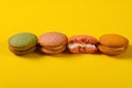 Colorful macaroons with one piece half eaten on yellow background