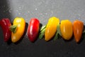 colorful mini peppers and mint leaves on black sunny background. Above view of yellow, red and orange peppers Royalty Free Stock Photo