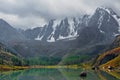 Colorful misty landscape with a turquoise mountain lake among snowy mountains under low cloudy sky in changeable weather. Stunning