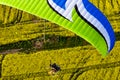 Colorful motorized paramotor flying freely over yellow rapeseed fields in spring