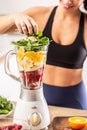 Colorful nutrition of spinach, oranges, bananas and strawberries put into a blender by a fit woman