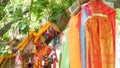 Colorful offering clothes on tree near altar. Bunch of bright traditional clothes as gift to Thai spirits hanging on tree branches