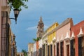 Colorful old buildings and street lamps line a street with a church tower emerging overhead in Campeche