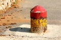 Colorful old dilapidated partially rusted concrete and metal parking security barrier or bollard mounted on asphalt to prevent