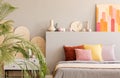 Colorful painting above bed with cushions in grey bedroom interior with palm. Real photo Royalty Free Stock Photo