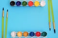 Colorful paints in jars on a blue background near the brushes. Color palette. Concept-creativity and school theme