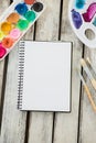 Colorful palette, paintbrushes and blank book on wooden surface