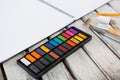 Colorful palette, paintbrushes and book on wooden surface