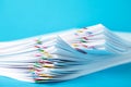 Colorful paper clip with pile of overload white paperwork on blue